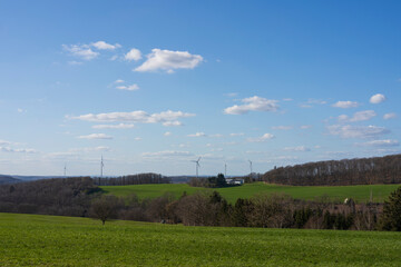 Panoramic photo of wind turbine park standing on a hill in spring against blue sky and white clouds. Green energy concept