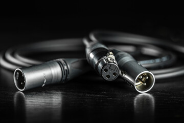 Close up of xlr audio cable connectors lying on a dark wooden surface