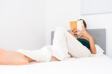 Portrait of a woman reading a book with mock text sitting on the bed relaxed and dressed casually....