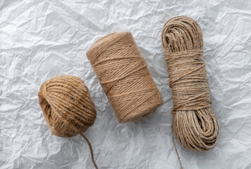 Roll of natural jute twine, on white crumpled paper background. Supplies for DIY crafts, hobby and...