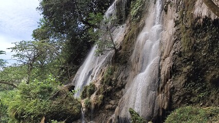 Fototapeta premium Serene Waterfall Cascading Through Lush Greenery, Tropical Paradise, Beautiful Natural Scenery
