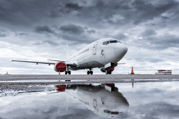 White passenger aircraft at airport with reflection in puddle in cloudy weather