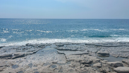 Clear view of the Mediterranean Sea from the rocky shore in Alanya, Turkey. Sunlight sparkles on the gentle waves under a bright summer sky. Peaceful coastal landscape.