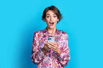 Photo of lovely astonished girl hold smart phone open mouth unbelievable news isolated on blue...