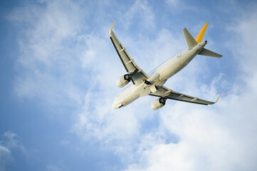 White commercial passenger jet flying in blue sky, bottom view. Unmarked airplane taking off or landing. Air travel concept, air transportation