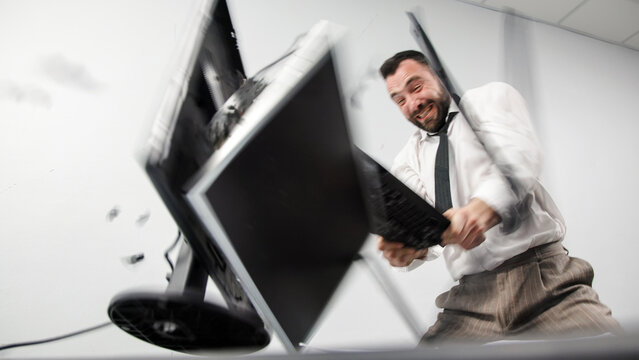 A businessman in aggression loses his temper in a fit of rage. An angry office worker smashes a computer monitor with his keyboard. Financial crisis or layoff. Motion blur.