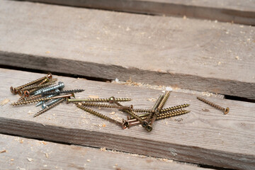 Many different self-tapping screws fasteners lie on a wooden table. Fasteners for making a roof.