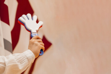 A fan's sports toy is a noisy hand with fingers in a woman's hand, red-white-blue on a beige background.