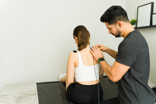 Male physiotherapist applying electrode pads to female patient's back during transcutaneous electrical nerve stimulation therapy treatment