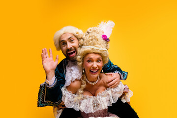 Cheerful couple representing aristocratic figures in vibrant costumes against a bright yellow background