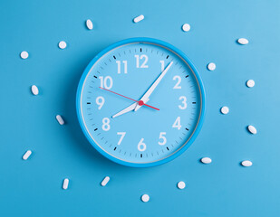 White pills on a blue background and a blue clock as a reminder.