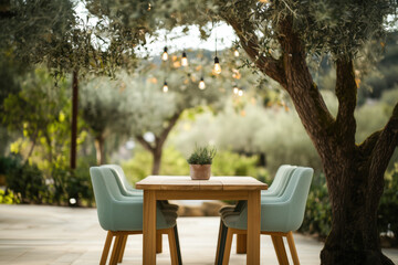 Fototapeta premium Outdoor dining area with wooden table and soft chairs under olives trees with glowing garlands