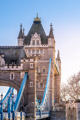 Tower Bridge showcases its intricate architecture against a blue sky. The historic structure features distinctive towers and vibrant blue cables, highlighting London's iconic skyline.