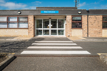 Outside view of a main entrance of a typical NHS hospital in Britain. Seen on the pedestrian crossing leading to the automatic double doors.