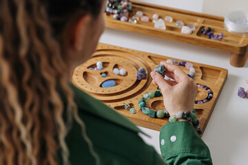 Jewelry maker assembling natural stone bracelets. Handmade beaded bracelet workshop with gemstones. Crafting spiritual gemstone jewelry. Natural stone.   