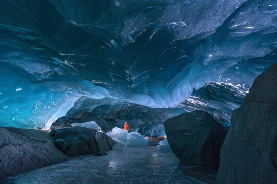 Inside of an ice cave with a person in red cloth showing the scale of the cave size. Morteratsch Glacier in Swiss Alps. (March 2025)