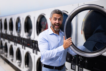 Busy man doing laundry and working on laptop. Stressed employee multitasking laundry and job. Tired...