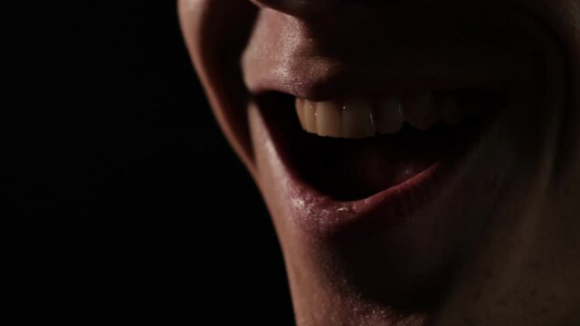 Close-up of angry laugh. Macro shot of mouth of a mad angry man smiling ominously on black background. A sinister gloating laugh.