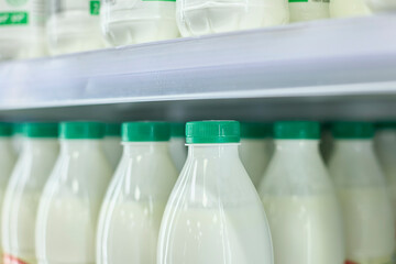 Bottles of milk with green caps arranged on a store shelf. Close-up view showcases uniformity and...