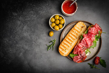 Salchichon extra or salami sandwich, grilled grain bread, with tomatoes and olives on dark...