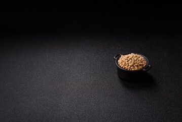 Peeled pine nuts in a bowl on a dark concrete background