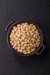 Peeled pine nuts in a bowl on a dark concrete background