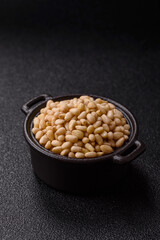 Peeled pine nuts in a bowl on a dark concrete background