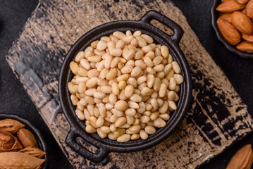 Peeled pine nuts in a bowl on a dark concrete background