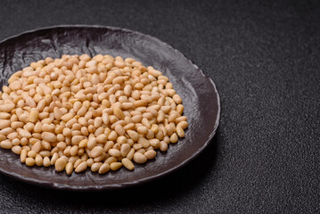 Peeled pine nuts in a bowl on a dark concrete background
