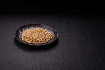 Peeled pine nuts in a bowl on a dark concrete background