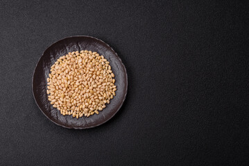 Peeled pine nuts in a bowl on a dark concrete background