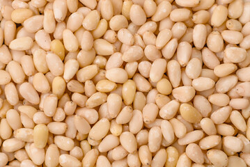Peeled pine nuts in a bowl on a dark concrete background