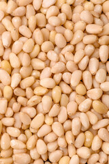 Peeled pine nuts in a bowl on a dark concrete background