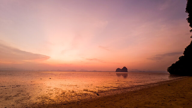 Stunning Sunset Over Tranquil Beach with Silhouetted Rock Formations and Vibrant Sky Reflections on Calm Water