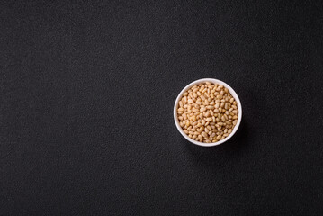 Peeled pine nuts in a bowl on a dark concrete background
