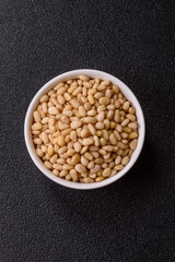 Peeled pine nuts in a bowl on a dark concrete background