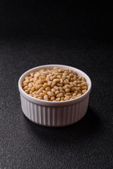 Peeled pine nuts in a bowl on a dark concrete background