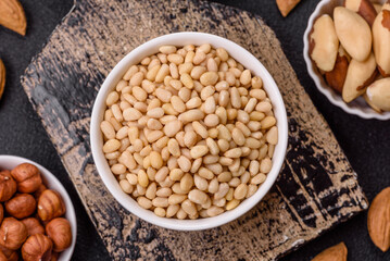 Peeled pine nuts in a bowl on a dark concrete background