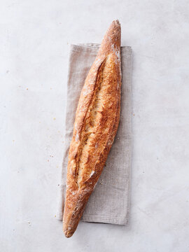 A beautiful loaf of freshly baked bread lies atop a soft linen napkin, radiating warmth and rustic charm. The golden crust showcases its artisanal quality, ready to be enjoyed