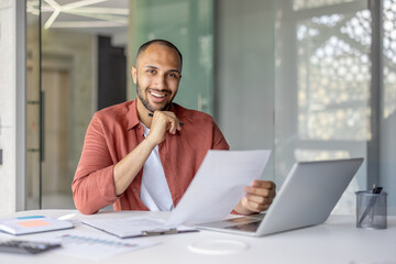 Portrait of a joyful successful financier, a man behind paperwork smiling and looking at the...