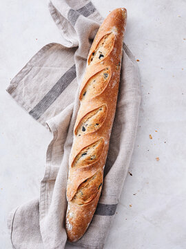 Warm, crusty baguette lies on a textured cloth, inviting and aromatic, as daylight filters softly through the kitchen window, enhancing the homey atmosphere
