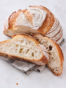 Warm, freshly baked artisanal bread showcases a beautifully scorched crust with intricate patterns. Soft slices reveal a fluffy, airy texture, resting gracefully on a light linen napkin