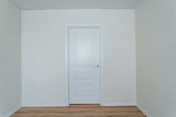 In the middle of the house, there exists an empty room which features a simple yet elegant white door alongside a charming wooden floor that enhances the overall appearance of the space