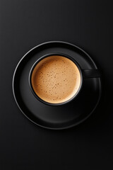 Fototapeta premium Overhead shot of steaming coffee with foamy surface served in a dark cup and saucer on a black backdrop