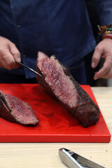 chef mostrando un secreto ibérico de cerdo asado poco hecho en una tabla de cocina con cuchillo en sus manos