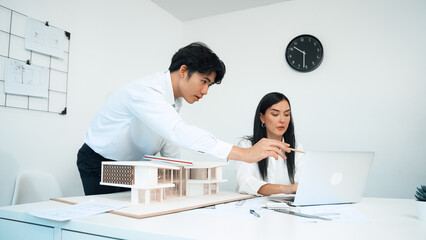 Professional male asian architect using ruler to measure house model length while young beautiful...