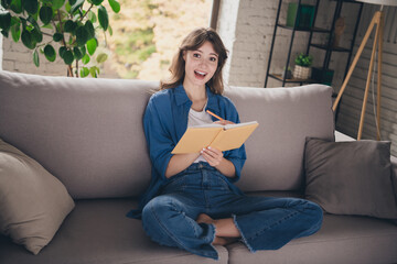 Young woman smiling while writing in a notebook, sitting on a cozy couch in a bright living room