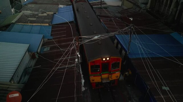 Train passing through Maeklong Railway Market in Thailand, squeezing between market stalls with goods just inches from the tracks