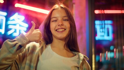 Smiling glad Caucasian Asian kid teenager junior demonstrating thumb up child agree in city...