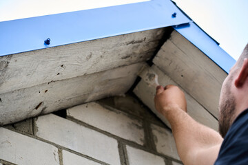 A man is painting a roof. The roof is made of wood and has a blue tarp